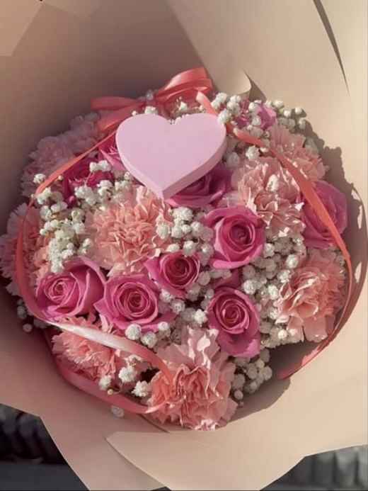 Pink roses and peach carnations with gypsophila, a coral ribbon and a pink heart topper, in blush wrap