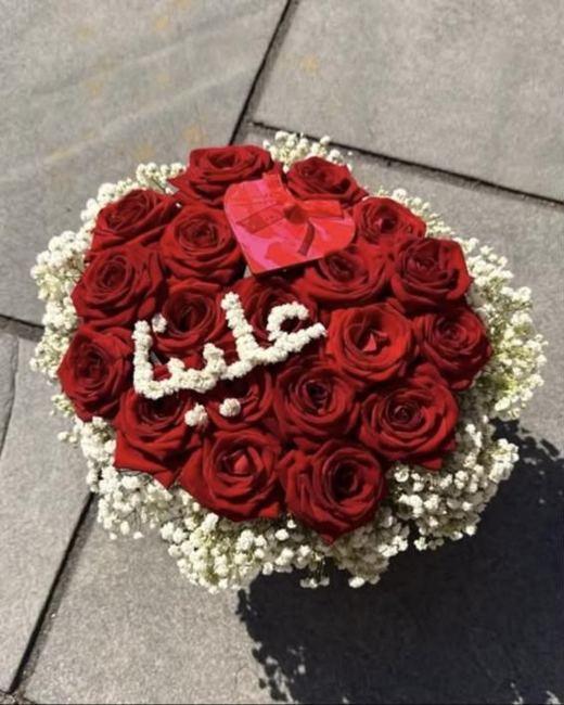 Heart-shaped arrangement of red roses ringed with gypsophila, with a name in gypsophila